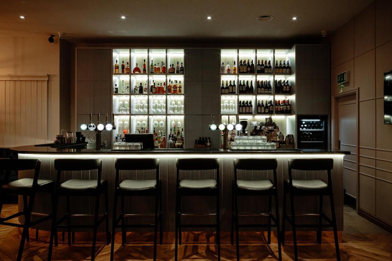 Citysuites Aparthotel Manchester Esterno foto The photo shows a modern bar setup. In the background, there is a well-organized shelf displaying a variety of bottles, illuminated with soft lighting, which creates an inviting atmosphere. The bar counter itself is sleek and minimalistic, with sever
