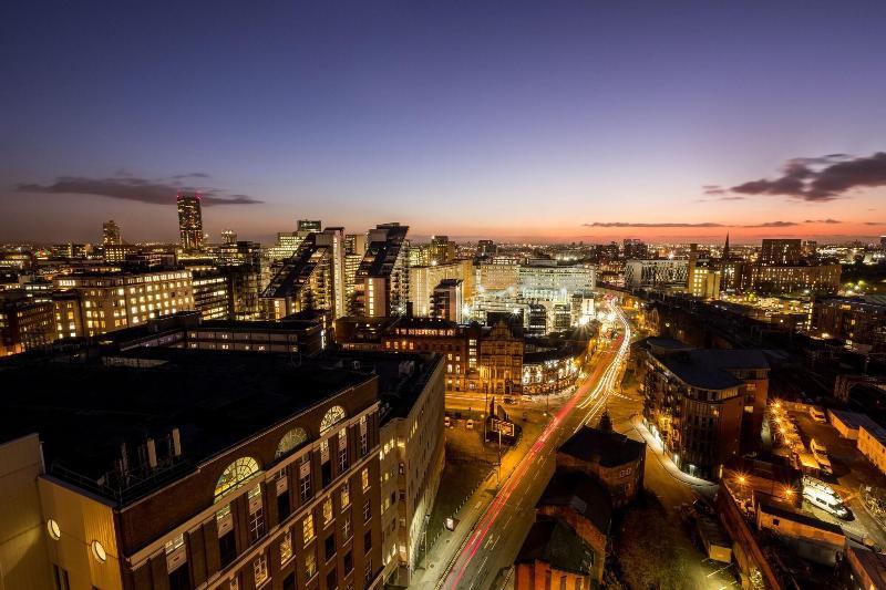 Citysuites Aparthotel Manchester Esterno foto The photo shows a panoramic view of a city during twilight. The skyline is dotted with a variety of modern buildings, showcasing a mix of architectural styles. Streets can be seen winding through the city, illuminated by streetlights and vehicle head
