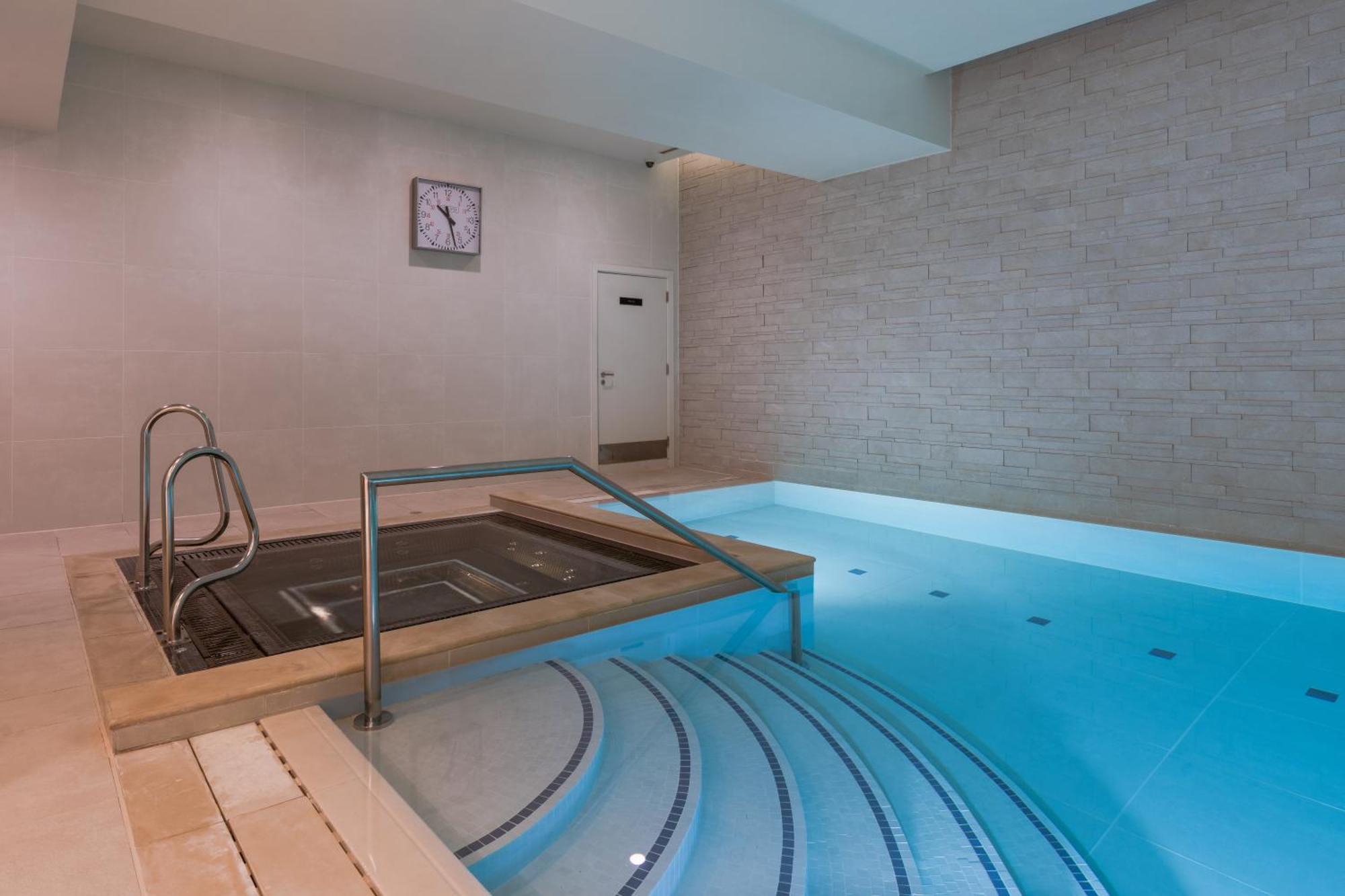 Citysuites Aparthotel Manchester Esterno foto The photo shows a modern spa area featuring a small indoor pool and a hot tub. The pool is designed with a light blue color, and there are steps leading down into it. Next to the pool, there is a hot tub with a stainless steel railing for access. The