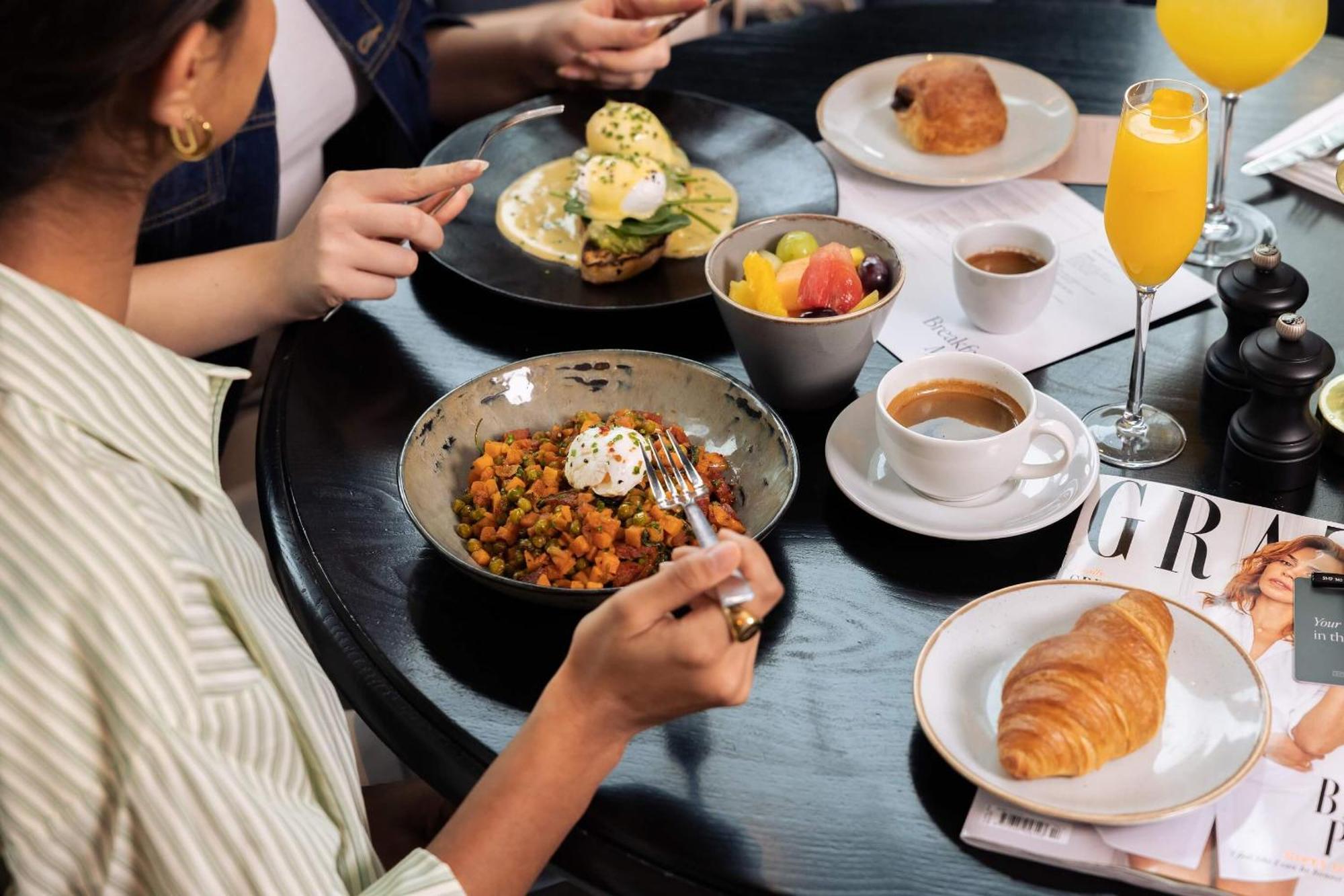 Citysuites Aparthotel Manchester Esterno foto The photo portrays a dining setting with several dishes and drinks. In the foreground, a person is holding a fork, poised to eat from a bowl filled with a colorful mixture that appears to include vegetables and garnished with a dollop of cream. 

Nea