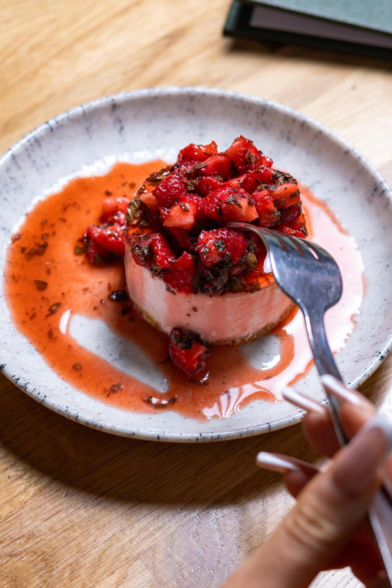 Citysuites Aparthotel Manchester Esterno foto The photo showcases a dessert that features a round, creamy base topped with a generous portion of strawberries. The strawberries appear to be fresh and are drizzled in a reddish syrup, which may also include some chocolate or other flavors. A fork i