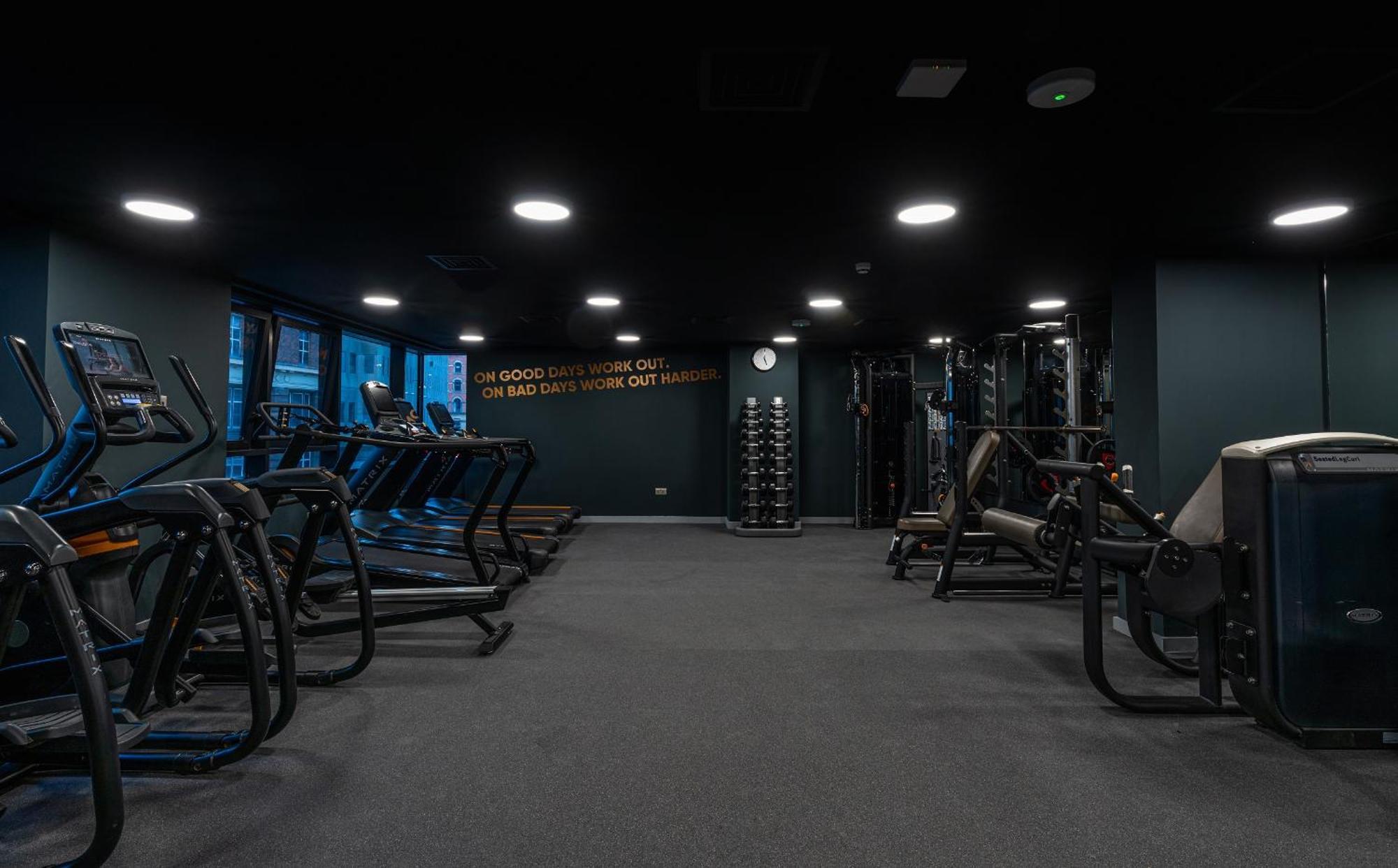 Citysuites Aparthotel Manchester Esterno foto The photo shows an interior view of a gym. There are several fitness equipment pieces arranged in the space, including treadmills and weight machines. The gym features dark-colored walls and flooring, contributing to a sleek, modern look. Natural lig