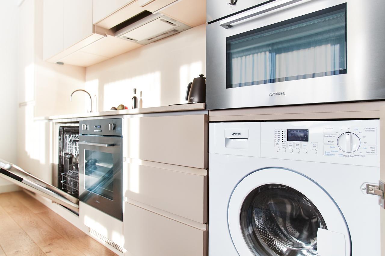 Citysuites Aparthotel Manchester Esterno foto The photo shows a modern kitchen area featuring several appliances. On the left side, there is a built-in dishwasher beneath a countertop. Next to it is an oven, also built into the cabinetry. To the right, there is a washing machine with a visible f