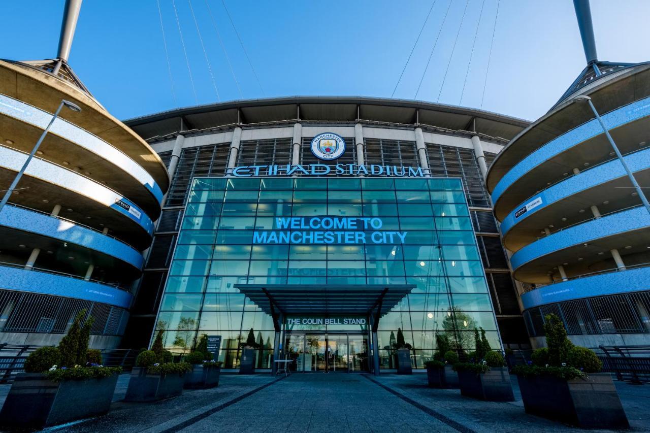Citysuites Aparthotel Manchester Esterno foto The image shows the entrance of the Etihad Stadium, which is the home of Manchester City Football Club. The facade features large glass panels with the club's logo prominently displayed at the top. A sign reads "WELCOME TO MANCHESTER CITY." The desig