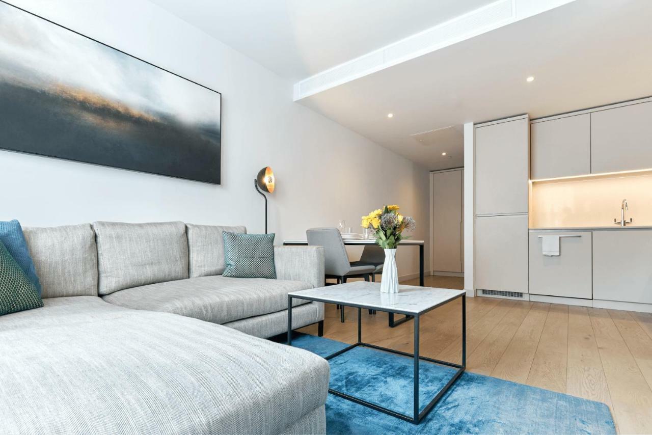 Citysuites Aparthotel Manchester Esterno foto The photo depicts a modern living space featuring a light-colored sofa with blue and gray throw pillows. In front of the sofa, there is a stylish coffee table with a marble top and a black frame. A vase of fresh flowers adds a touch of color to the t