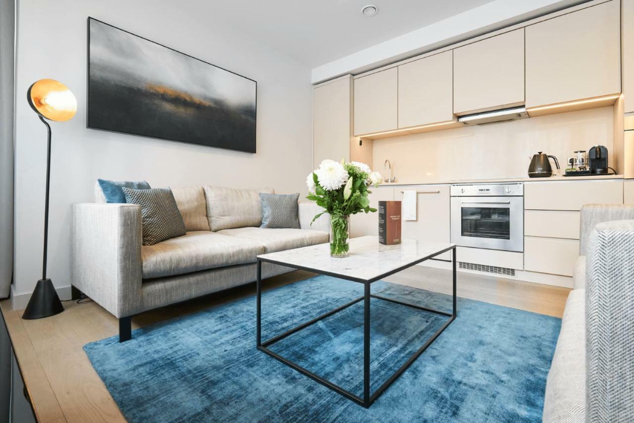 Citysuites Aparthotel Manchester Esterno foto The photo shows a modern living space with a cozy and contemporary design. There is a light grey sofa with plush cushions, positioned in front of a sleek coffee table with a black metal frame. On the table, there is a vase with fresh flowers, adding 