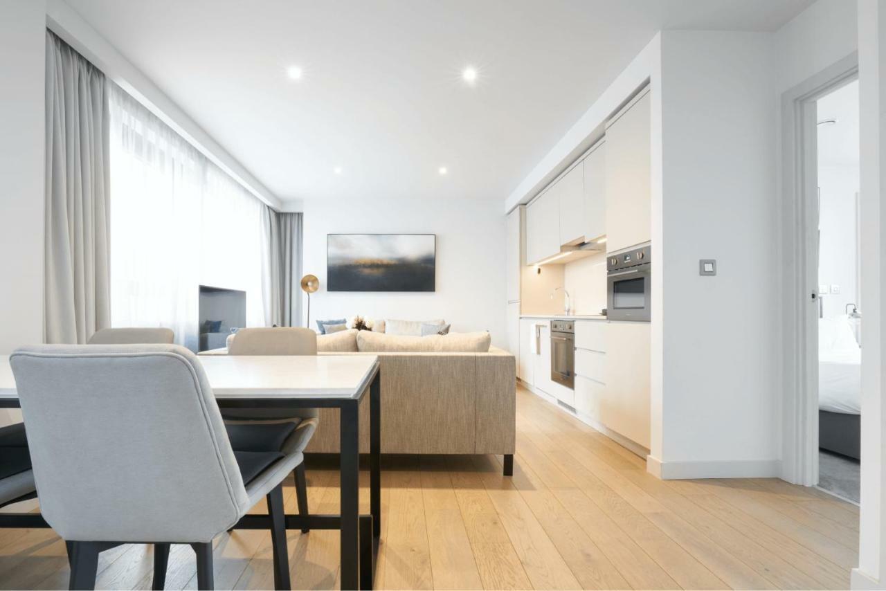 Citysuites Aparthotel Manchester Esterno foto The photo shows a modern and airy living space with a light color palette. In the foreground, there's a dining table with sleek chairs. The room features a cozy seating area with a sofa that faces a wall-mounted television. To the right, there is a k